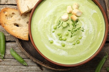 Tasty pea cream soup with croutons and thyme served on wooden table, flat lay