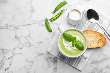 Tasty pea cream soup with basil served on white marble table, flat lay. Space for text