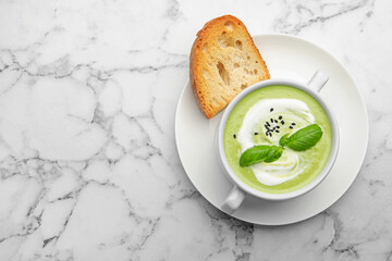 Tasty pea cream soup with basil served on white marble table, top view. Space for text