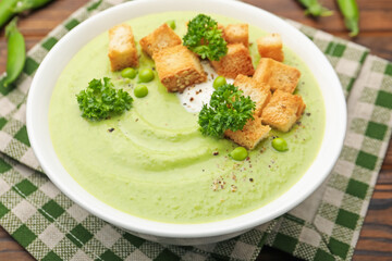 Tasty pea cream soup with croutons and broccoli served on wooden table, closeup