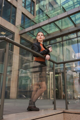 Girl with hot coffee against the background of a modern city building.