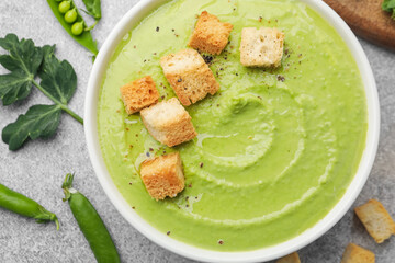 Tasty pea cream soup with croutons served on grey table, flat lay
