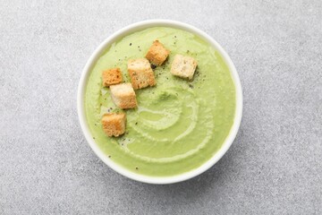 Tasty pea cream soup with croutons on grey table, top view