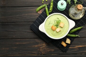 Tasty pea cream soup with croutons served on dark wooden table, flat lay. Space for text