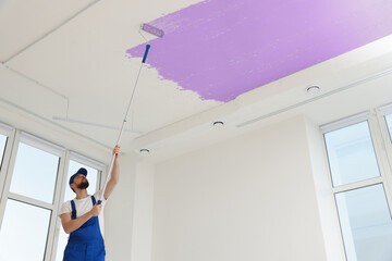 Man painting white ceiling with violet dye indoors, low angle view