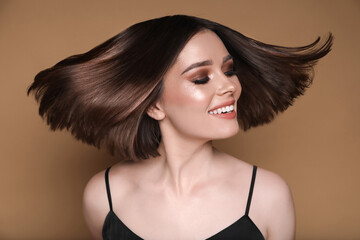 Beautiful young woman with shiny healthy hair on pale brown background
