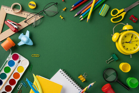 Colorful school supplies including a clock, notebooks, and stationery displayed against a green backdrop - Powered by Adobe