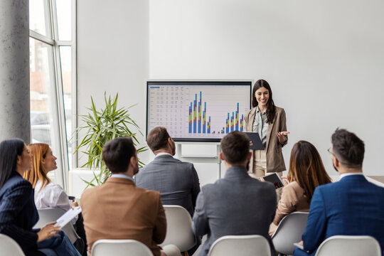 Young female data analyst with tablet in hands standing in front of auditorium at boardroom and presenting analytic and charts on whiteboard. - Powered by Adobe