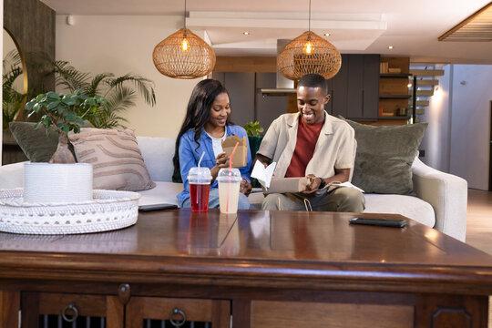 African American couple opening gift box and reading card in modern living room, with takeaway cups