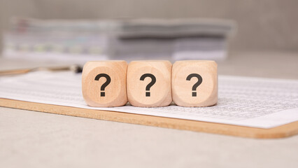 Three wooden cubes with question marks on financial papers, concept of uncertainty.