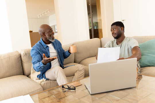 Discussing African American father and son reviewing documents on sofa, with coffee mug and laptop