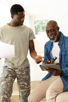 Smiling African American father and son comparing tablet and paper in living room, with eyeglasses