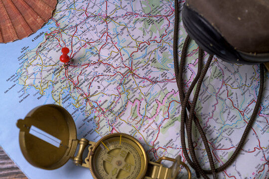 Hiking boots on a map on a wooden floor and rustic background with a compass and a scallop shell with the city of Santiago de Compostela marked.