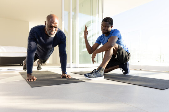 Performing push-ups African American trainer and client working out in home gym, with mats