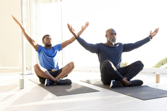 Meditating African American father and son sitting in studio, with yoga mats and water bottle