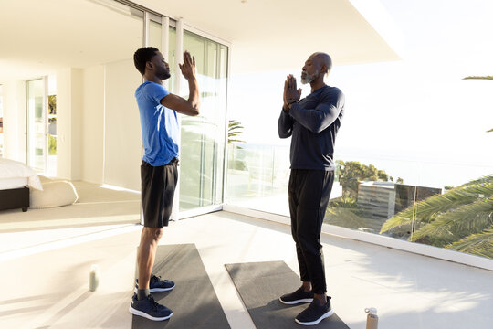 Practicing African American father and son doing yoga on mats in living room, with ocean view
