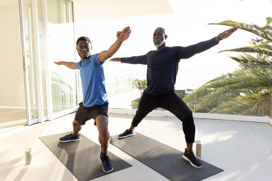 Practicing African American father and son doing yoga on glass balcony, with mats and water bottles