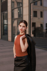 A girl with freckles in a leather skirt near a skyscraper.