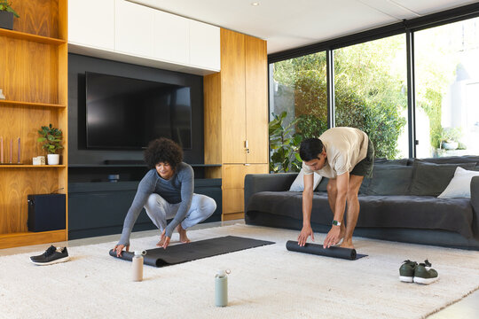 Unrolling yoga mats diverse male friends preparing living room workout on rug, with water bottles