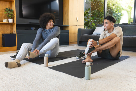 Diverse male friends stretching feet on yoga mats in living room, with insulated water bottles