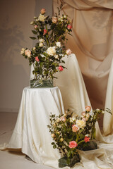 Elegant floral compositions of roses in soft pink and cream tones are placed on white-draped pedestals in a studio setting. Ideal for wedding planning, floral design, or romantic decor. 