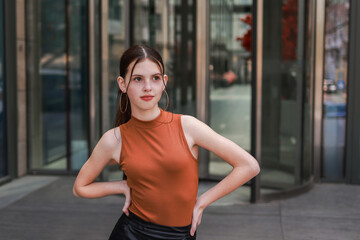 A girl with freckles in a leather skirt near a skyscraper.