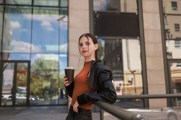 Girl with hot coffee against the background of a modern city building.