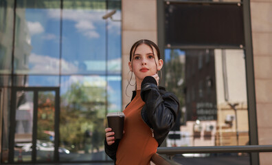 Girl with hot coffee against the background of a modern city building.