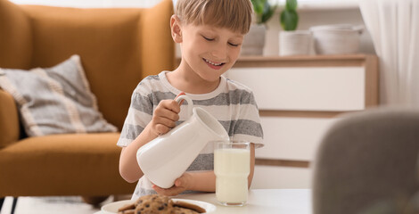 Cute little boy pouring milk into glass at home