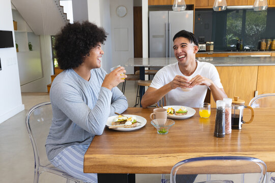 Sharing breakfast diverse male friends sitting at table in kitchen, with avocado toast and coffee - Powered by Adobe