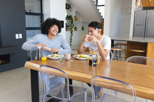 Diverse male friends sharing breakfast in home kitchen area, with avocado toast and French press - Powered by Adobe