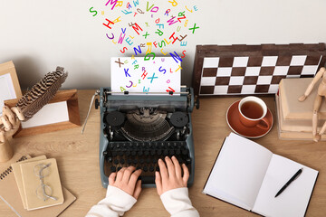 Female author typing on vintage typewriter at table in office, top view