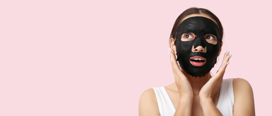 Surprised young woman with activated charcoal mask on her face against pink background
