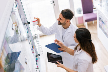 Obraz premium Pharmacists Selecting Medicine from Shelf Using Tablet in Pharmacy