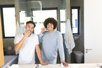 Diverse male friends brushing teeth at modern bathroom vanity, with toothbrushes and hanging towels