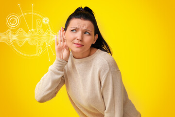 Young woman trying to hear something on yellow background