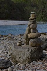 A delicate balance of stacked stones by the river, their textured surfaces glowing in soft natural light. Earthy tones, tranquil water, and an organic composition evoke harmony and quiet contemplation
