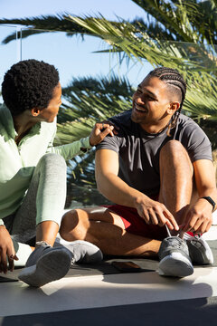Tying sneaker laces, diverse friends sitting on outdoor balcony mats, with smartphone between them