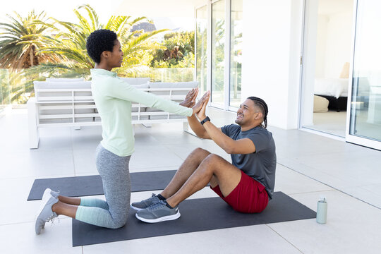 Practicing partner yoga Diverse friends pressing palms on sunny patio, with mats and water bottle
