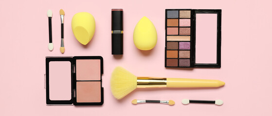 Makeup sponges with yellow brush and different decorative cosmetics on pink background