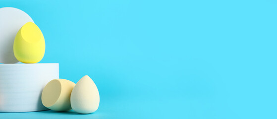 Decorative podiums with makeup sponges on blue background