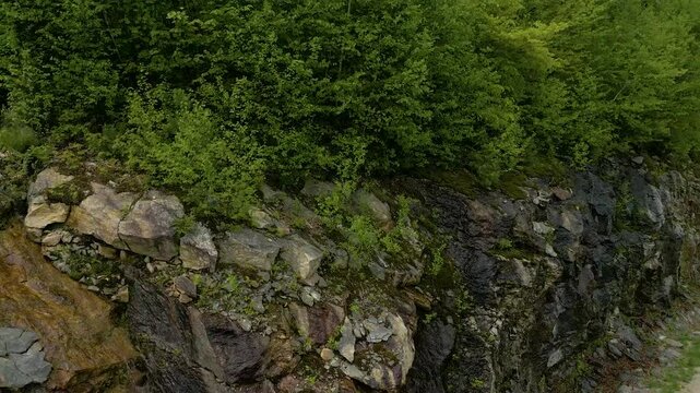 Wet Rock Face with Natural Mineral Streaks and Moss in Forested Terrain, Pans to Reveal Mountains, drone 4K