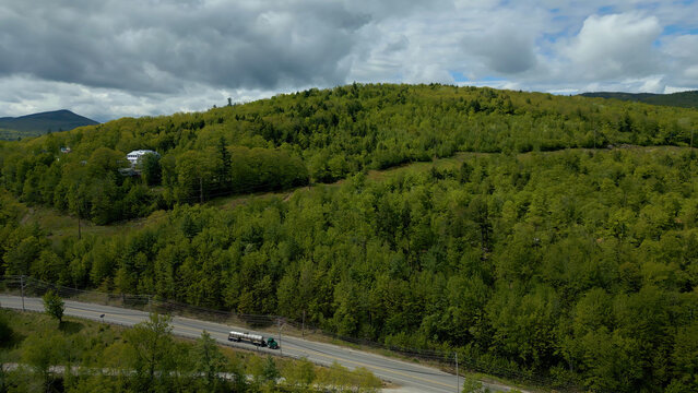 Aerial View of Forested Hillside in Maine with Truck on Rural Road Under Cloudy Sky