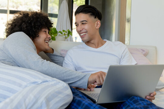 Sitting diverse male friends browsing online content on living room couch, with silver laptop - Powered by Adobe