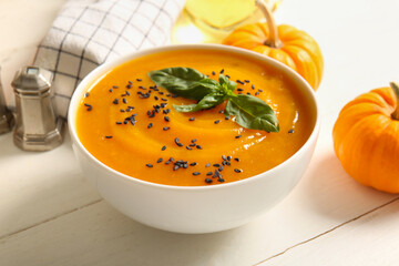 Bowl of delicious pumpkin cream soup with seeds and basil on white wooden table