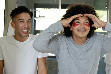 Applying red gel patches, diverse male friends standing at modern bathroom mirror with white towels