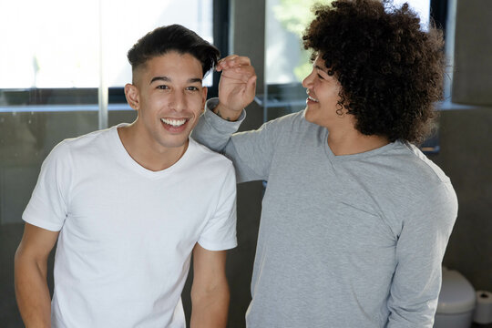 Smiling diverse male friends styling hair in bright modern bathroom, with white toilet - Powered by Adobe