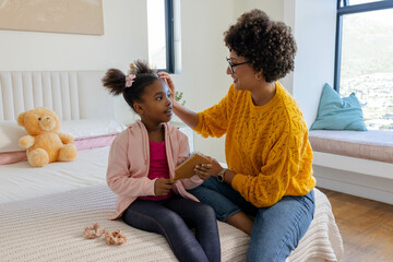 Diverse mother and African American child styling hair in child bedroom, with wooden hairbrush