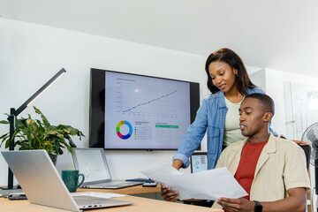 Reviewing African American coworkers studying documents at office desk, with monitor, copy space