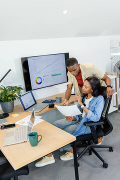 Reviewing African American colleagues analyzing reports at office desk, with mounted monitor